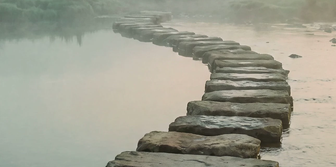 Stepping stones crossing still water in morning mist.
